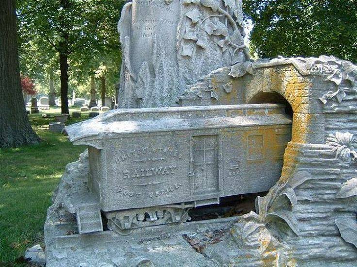 A detailed stone monument in a cemetery, depicting a train car emerging from a tunnel.