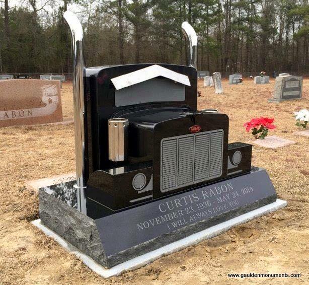 Black semi-truck-shaped tombstone in a cemetery; name and dates on the base.