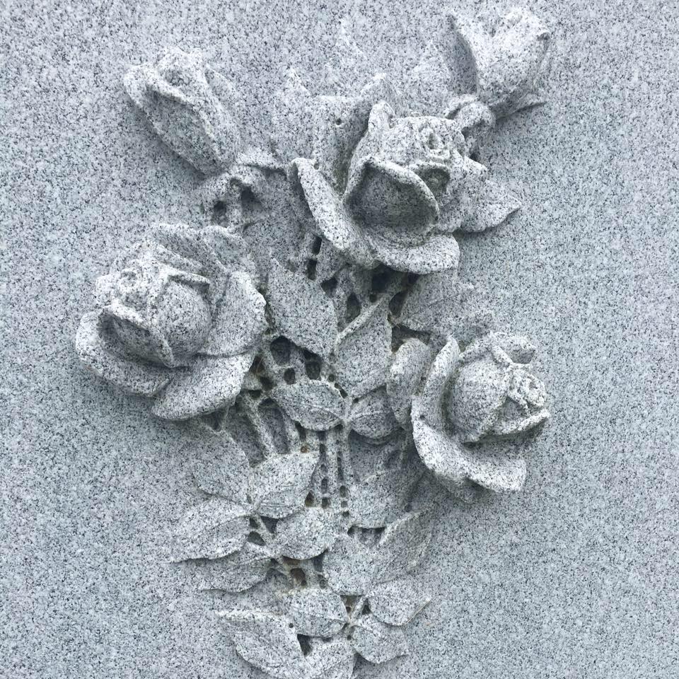 Sculpture de roses en pierre grise sur un fond texturé et moucheté.