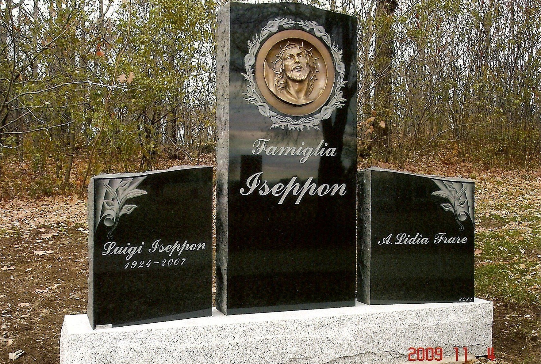 Black granite family headstone with engraved names, dates, and a central bronze medallion of Jesus.
