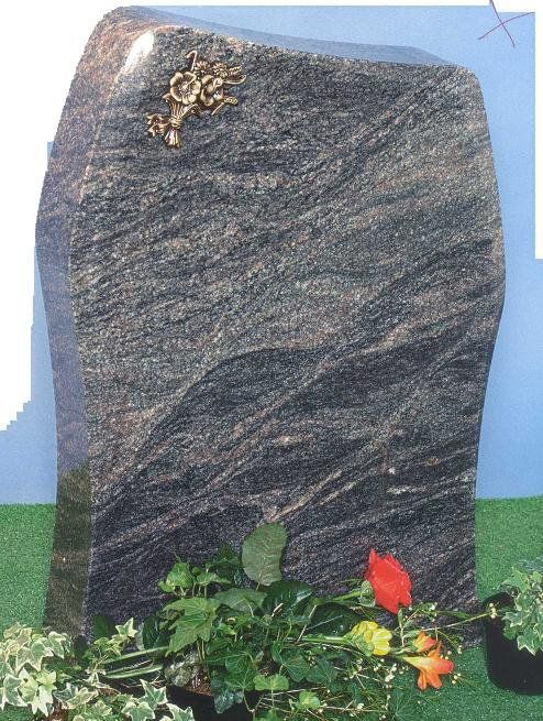 Granite headstone with bronze floral accent, resting on grass with red and orange flowers.