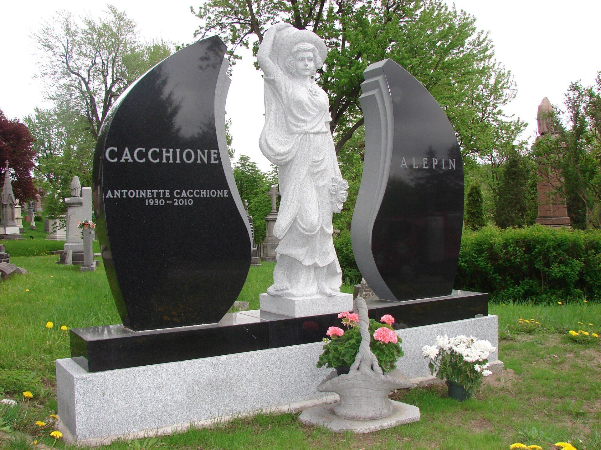 Elaborate black marble tombstone with white statue of a woman between two panels in a cemetery.