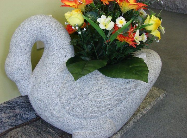 Swan-shaped granite planter holding colorful artificial flowers.