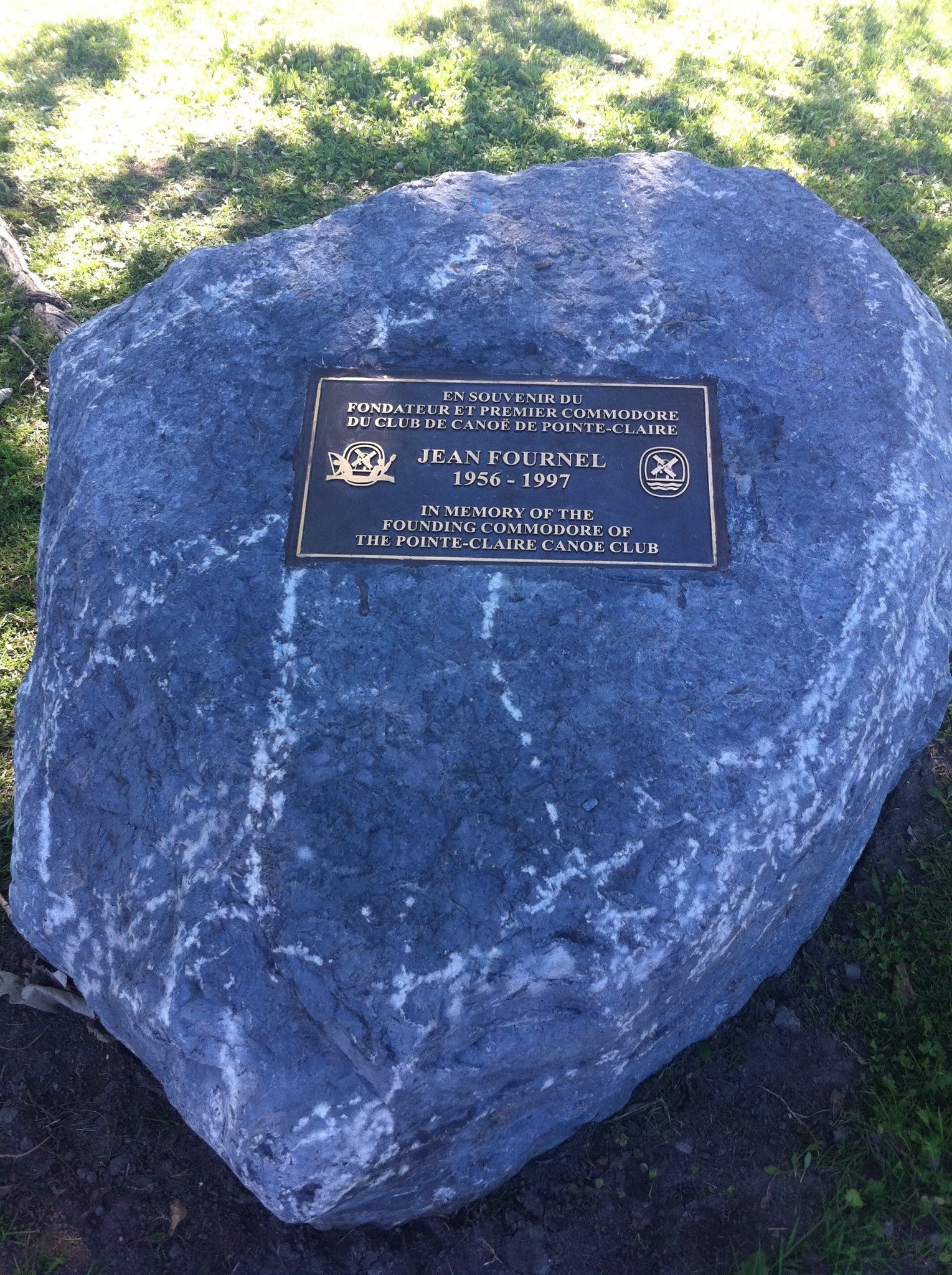 Large, dark gray boulder with a bronze plaque, set outdoors on grass. Plaque has text.