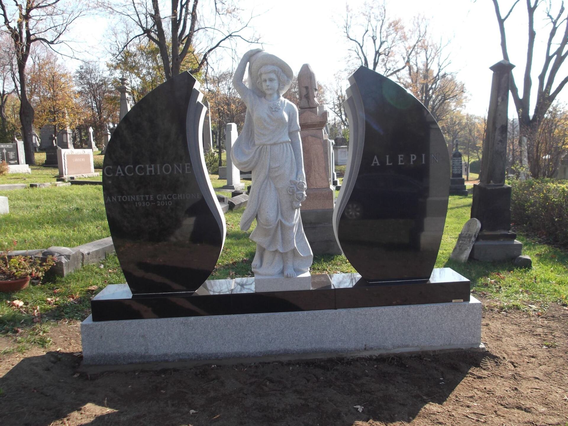 Monument with statue of a draped figure; black granite wings with names
