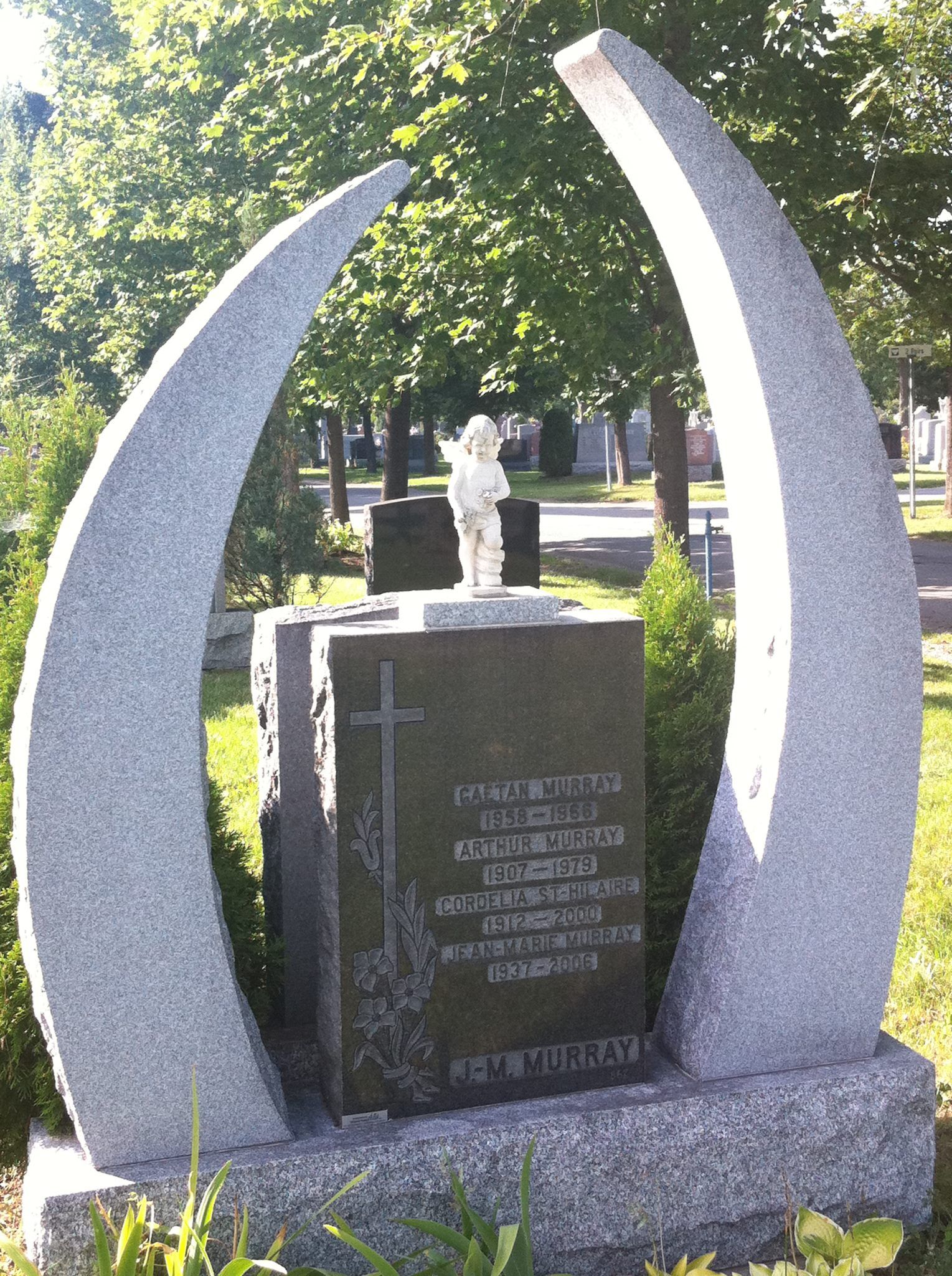 Pierre tombale en granit gris avec arches courbes, inscription et statue d'ange dans un cimetière.