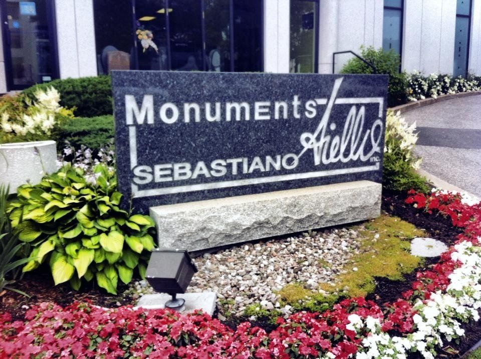 Panneau indiquant « Monuments Fields Sebastiano » dans un jardin, avec des fleurs éclatantes et de la verdure.