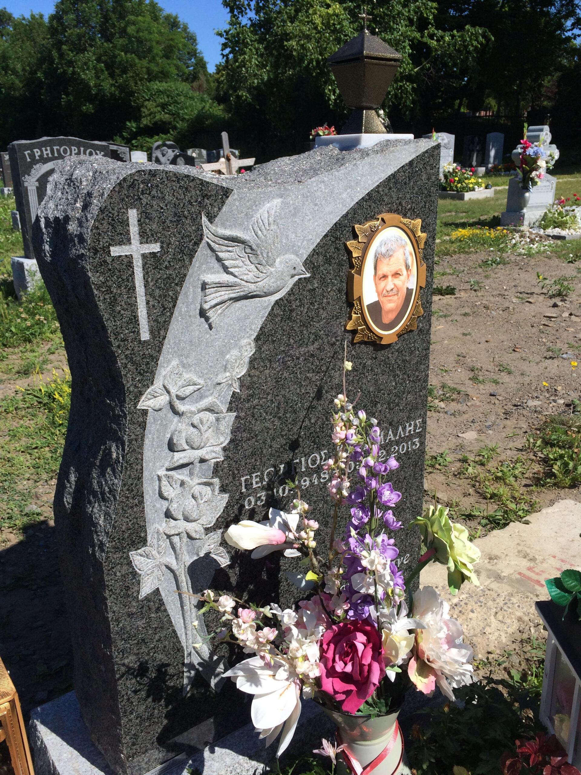 Granite headstone with cross, floral design, portrait, and flowers at a cemetery.