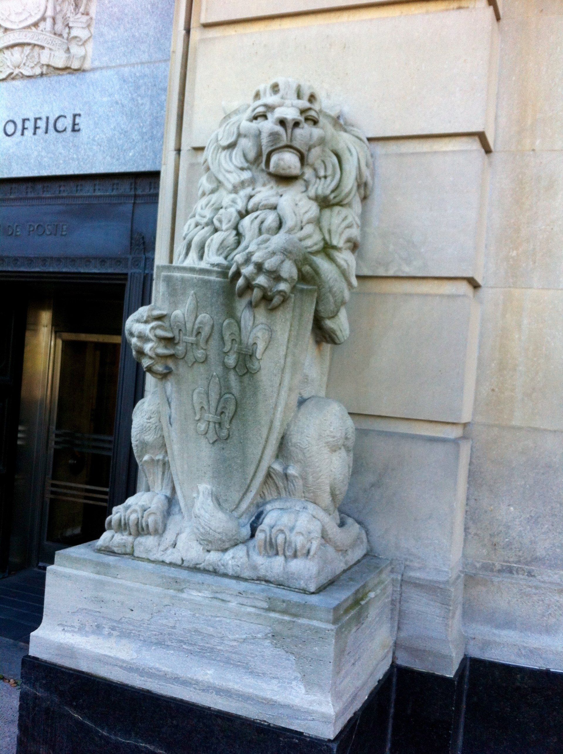 Stone lion statue holding a shield, outside a building with 