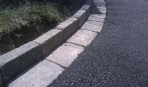 Stone curb and gutter alongside a dark asphalt road, with grass on the left.