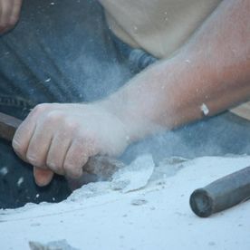 Person carving stone with a chisel; white dust in the air.