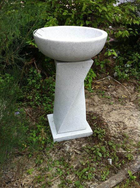 White stone birdbath with a bowl-shaped basin and a twisted pedestal, outdoors.