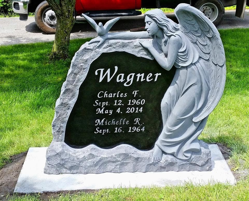 Une pierre tombale sur laquelle est appuyé un ange, gravée du nom « Wagner » ainsi que des noms et dates de Charles et Michelle.