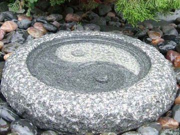 Bain d'oiseaux en pierre orné d'un motif Yin et Yang, entouré de galets.