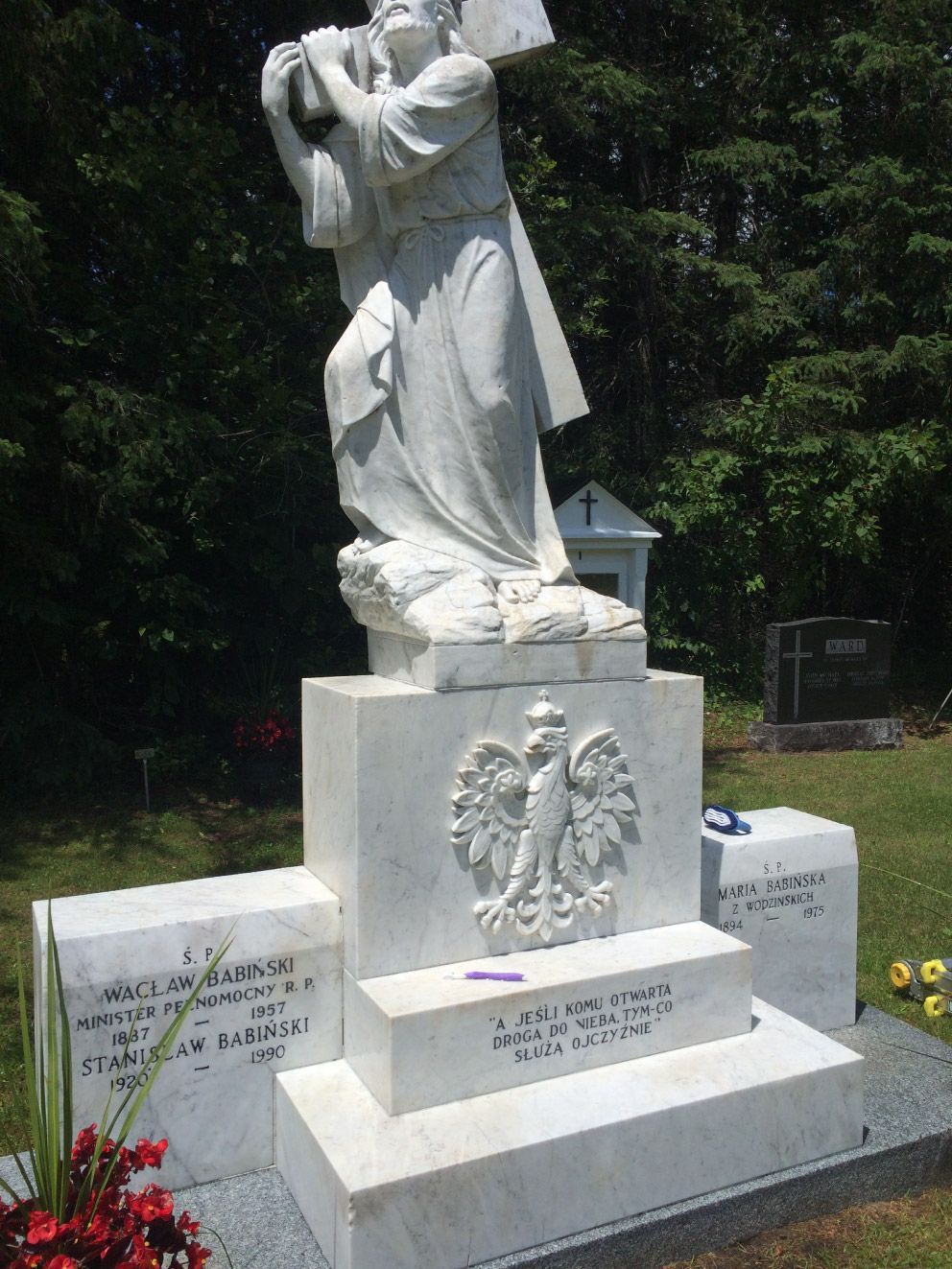White marble sculpture of a person carrying a cross atop a Polish memorial in a cemetery.