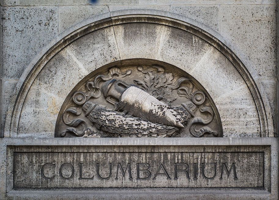 Sculpture en relief sur pierre au-dessus de « COLUMBARIUM » : Deux urnes à motifs floraux, placées dans une alcôve cintrée.