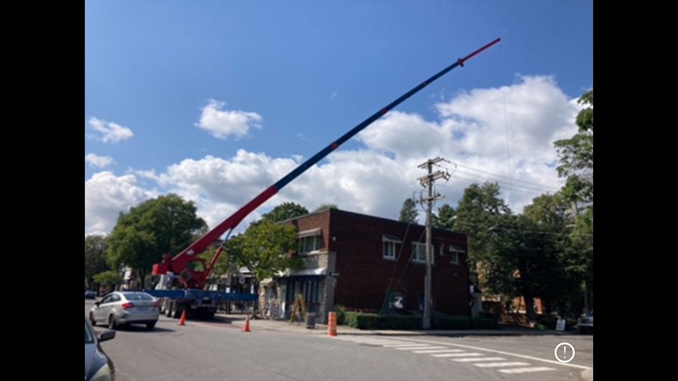 A red and blue crane is sitting on the side of the road in front of a building.