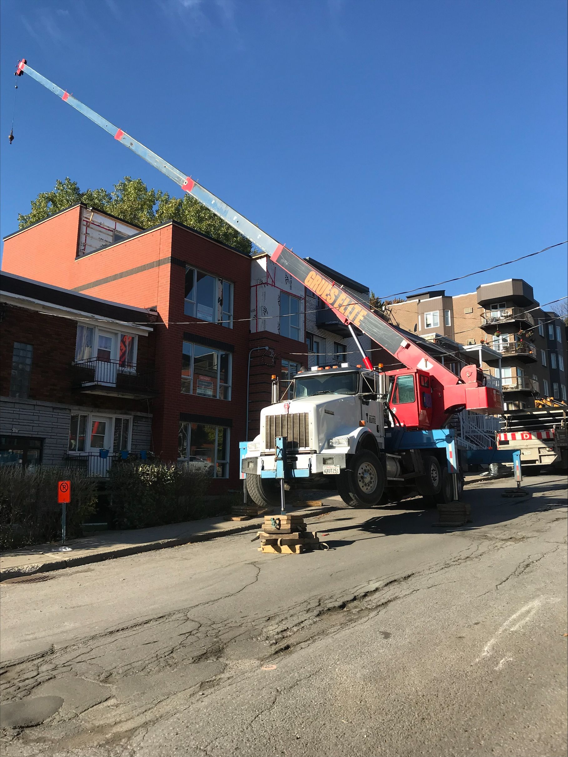 A truck with a crane attached to it is parked on the side of the road in front of a building.