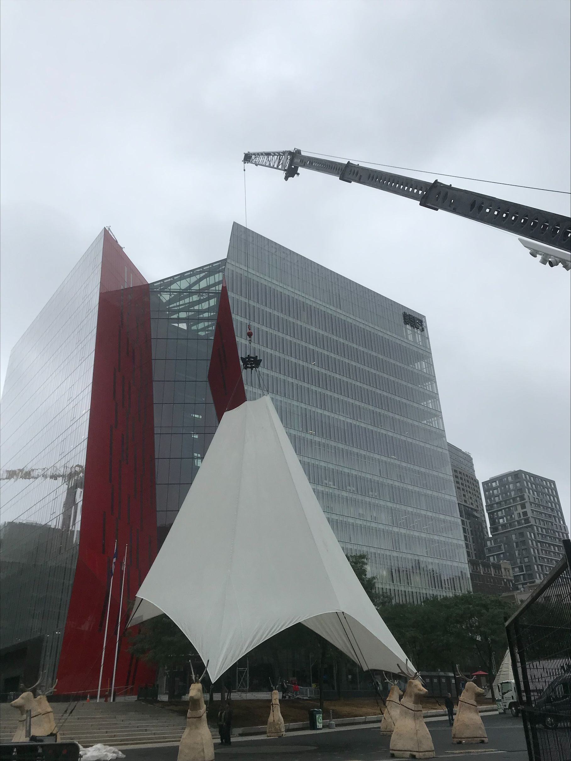 A crane is lifting a tent in front of a large building.