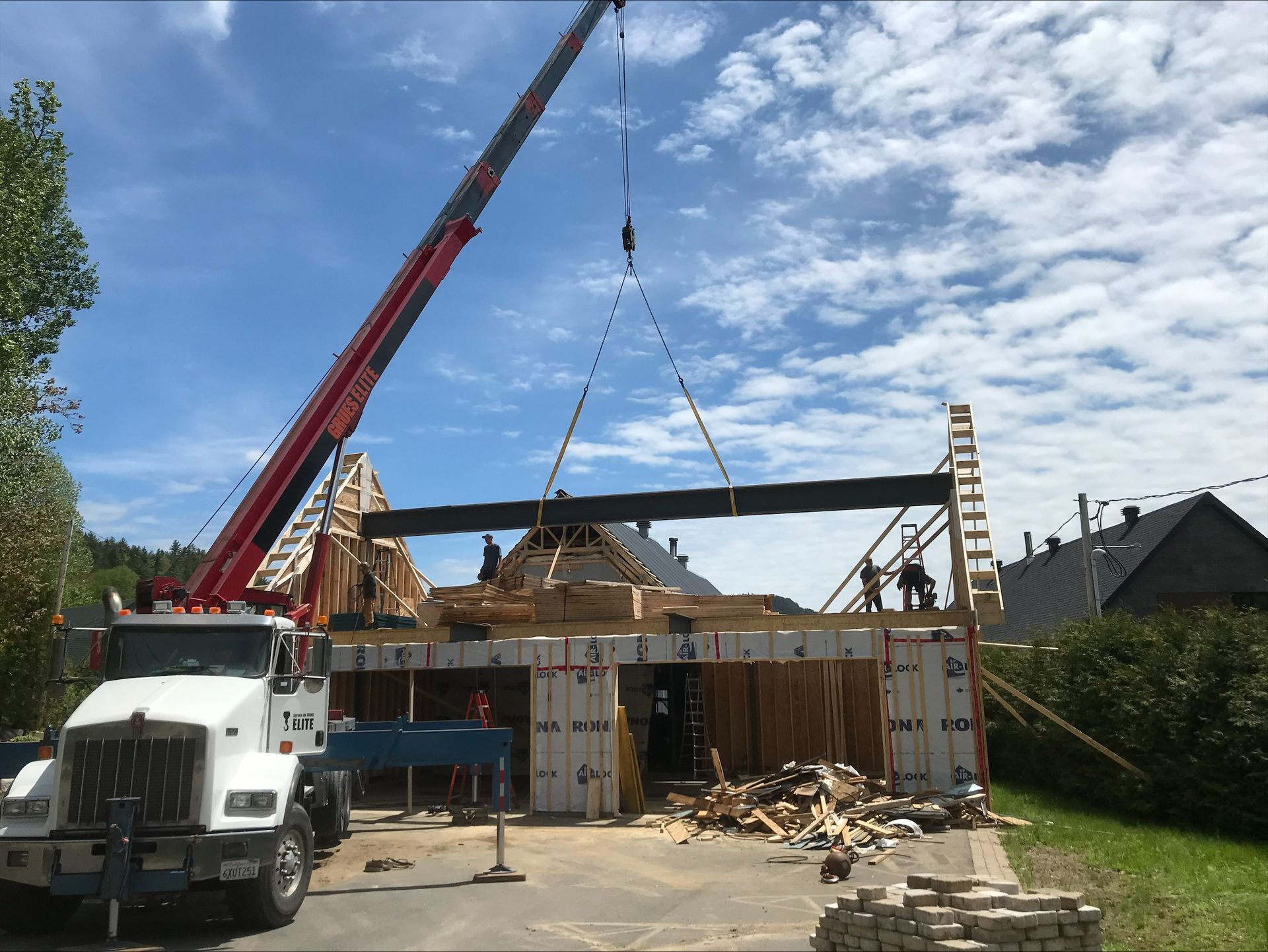 A crane is lifting a beam over a house under construction.