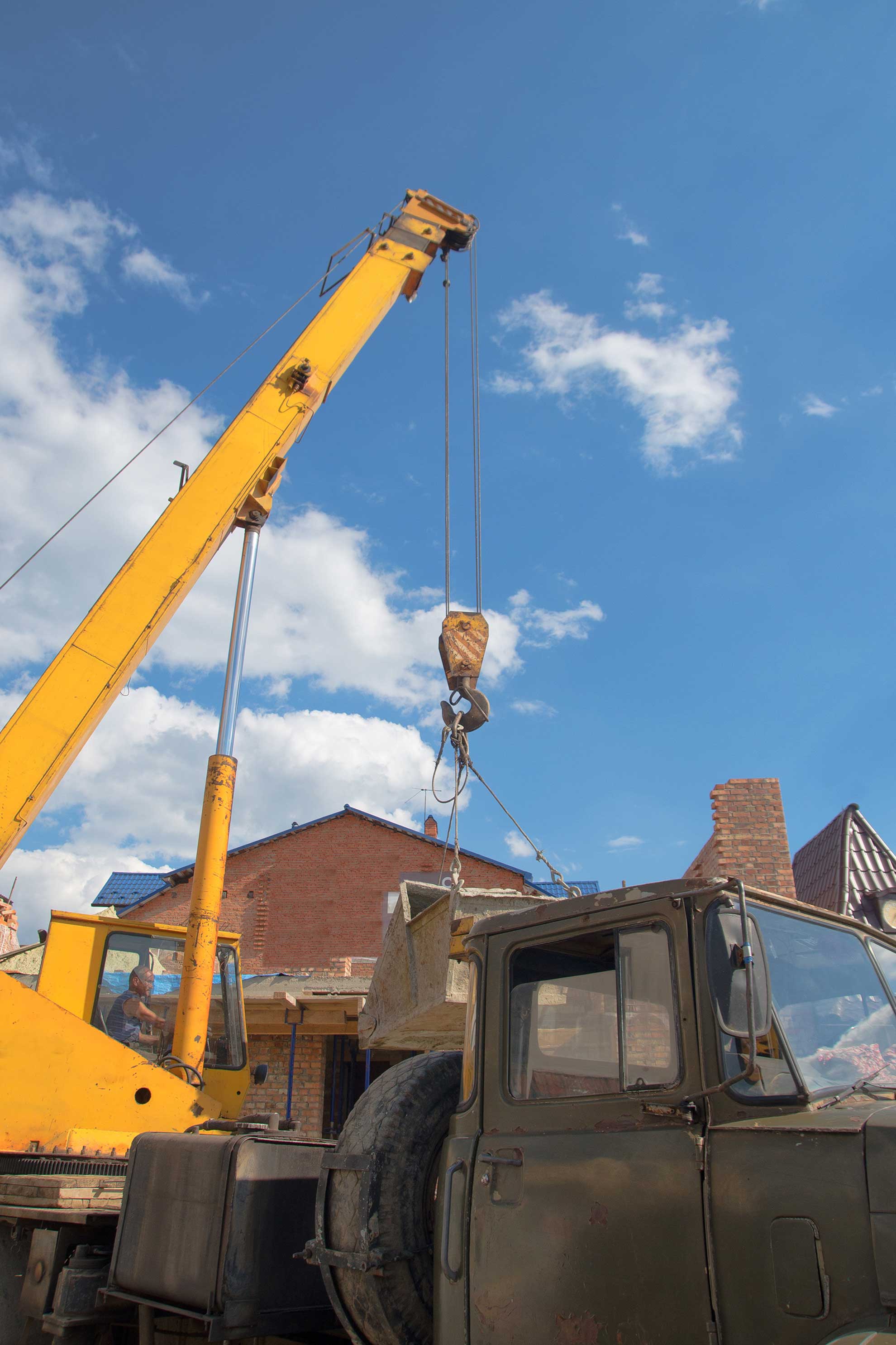 Grue jaune soulevant une charge près d'un bâtiment sous un ciel bleu.