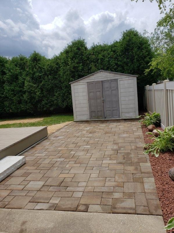 A shed is sitting in the backyard next to a brick walkway.