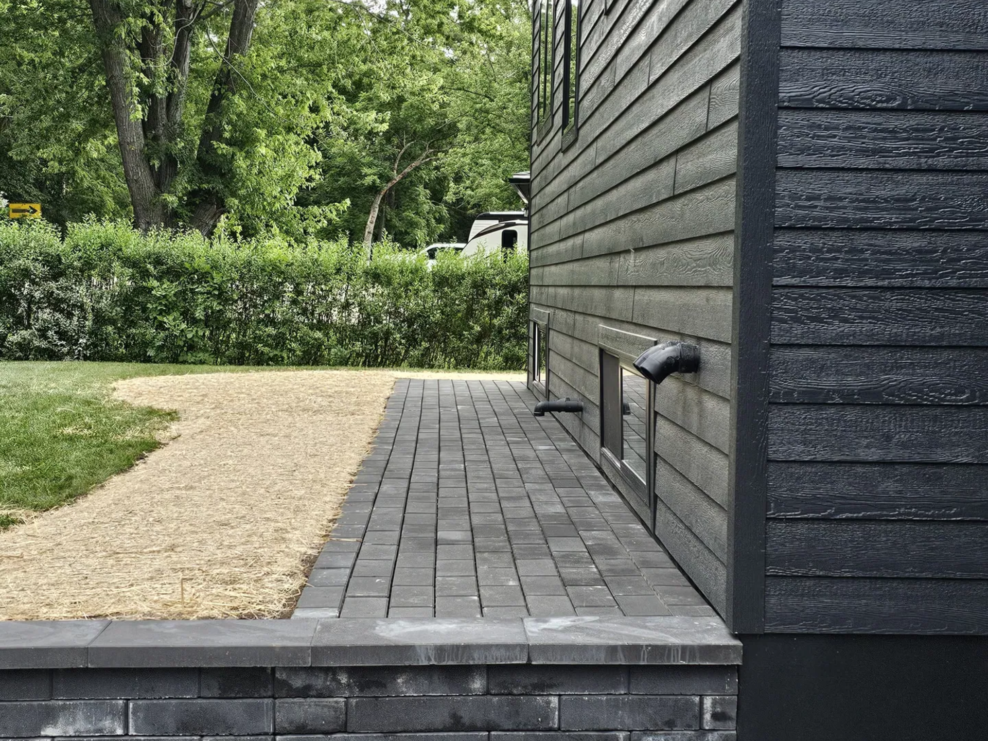 Charcoal paver walkway and matching retaining wall along the side of a modern black-sided home in Janesville, WI