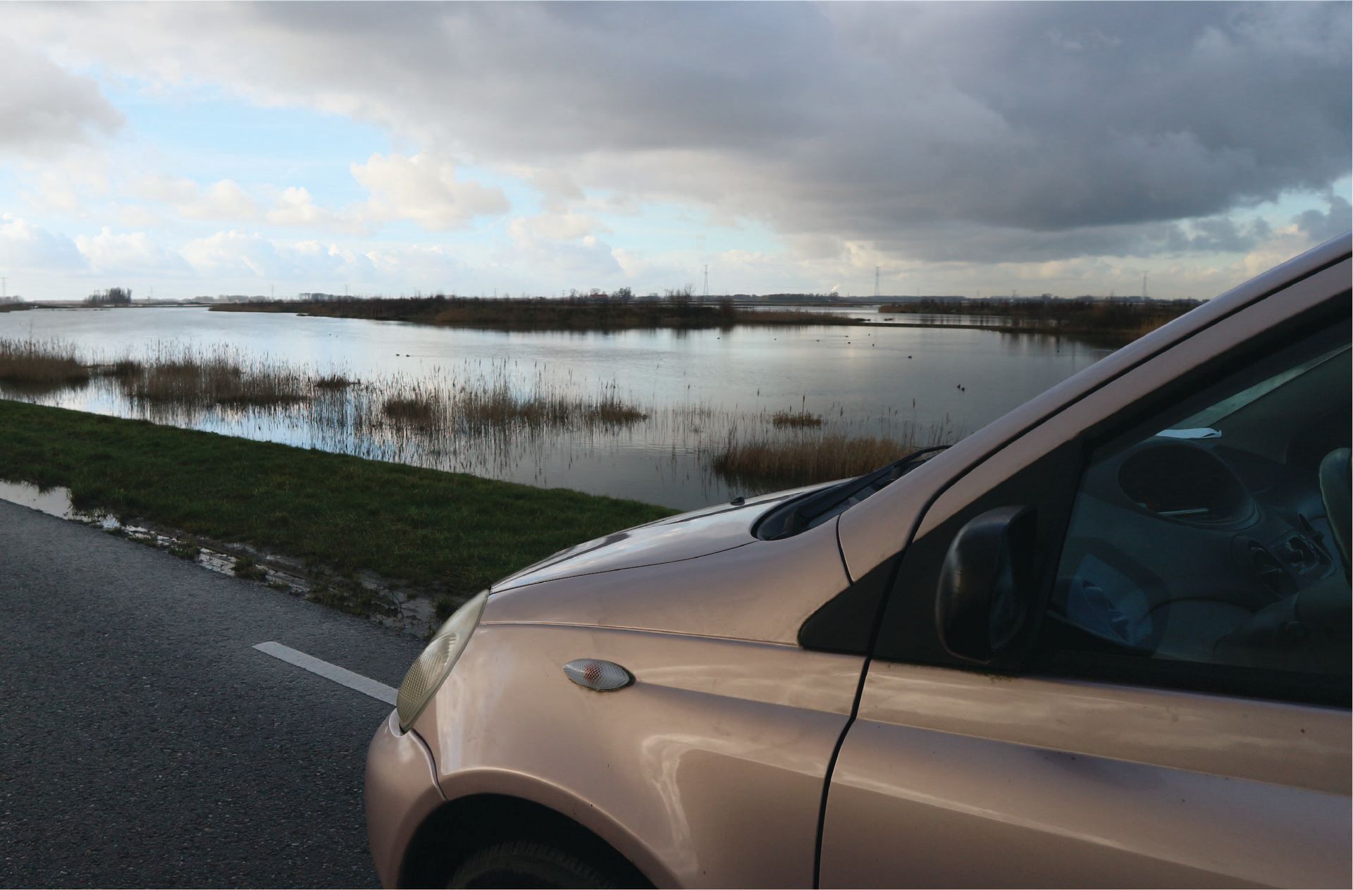 Een auto staat langs de kant van de weg geparkeerd naast een ondergelopen veld.