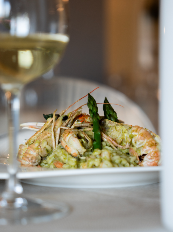 Pasta con gamberi grigliati su un piatto bianco, con un bicchiere di vino in primo piano.