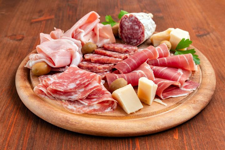 Un assortimento di salumi e formaggi disposti su un tagliere di legno con guarnizione di prezzemolo su un tavolo.