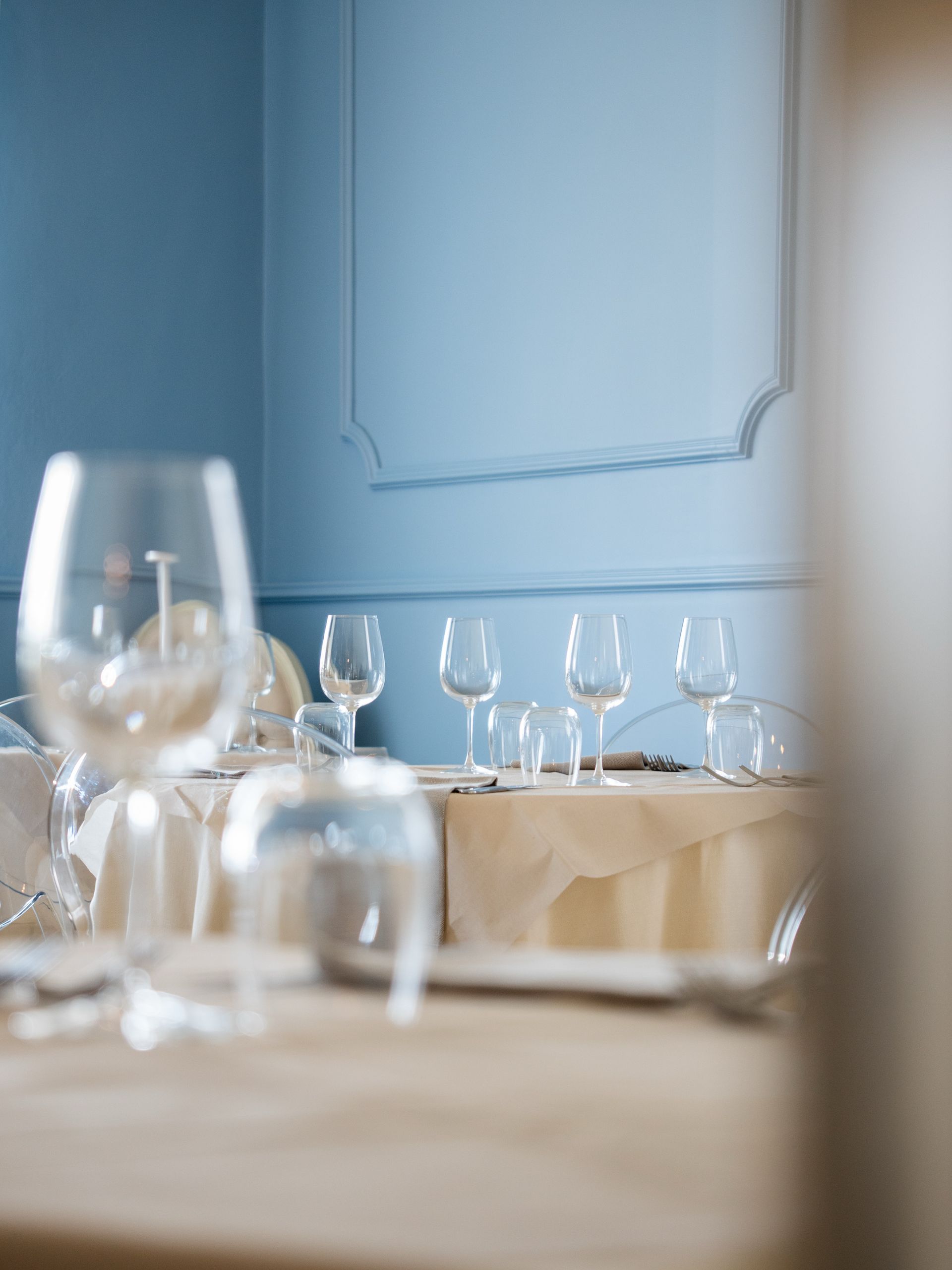 Calici da vino e tovaglioli piegati su un tavolo in una sala da pranzo illuminata da una luce blu soffusa.
