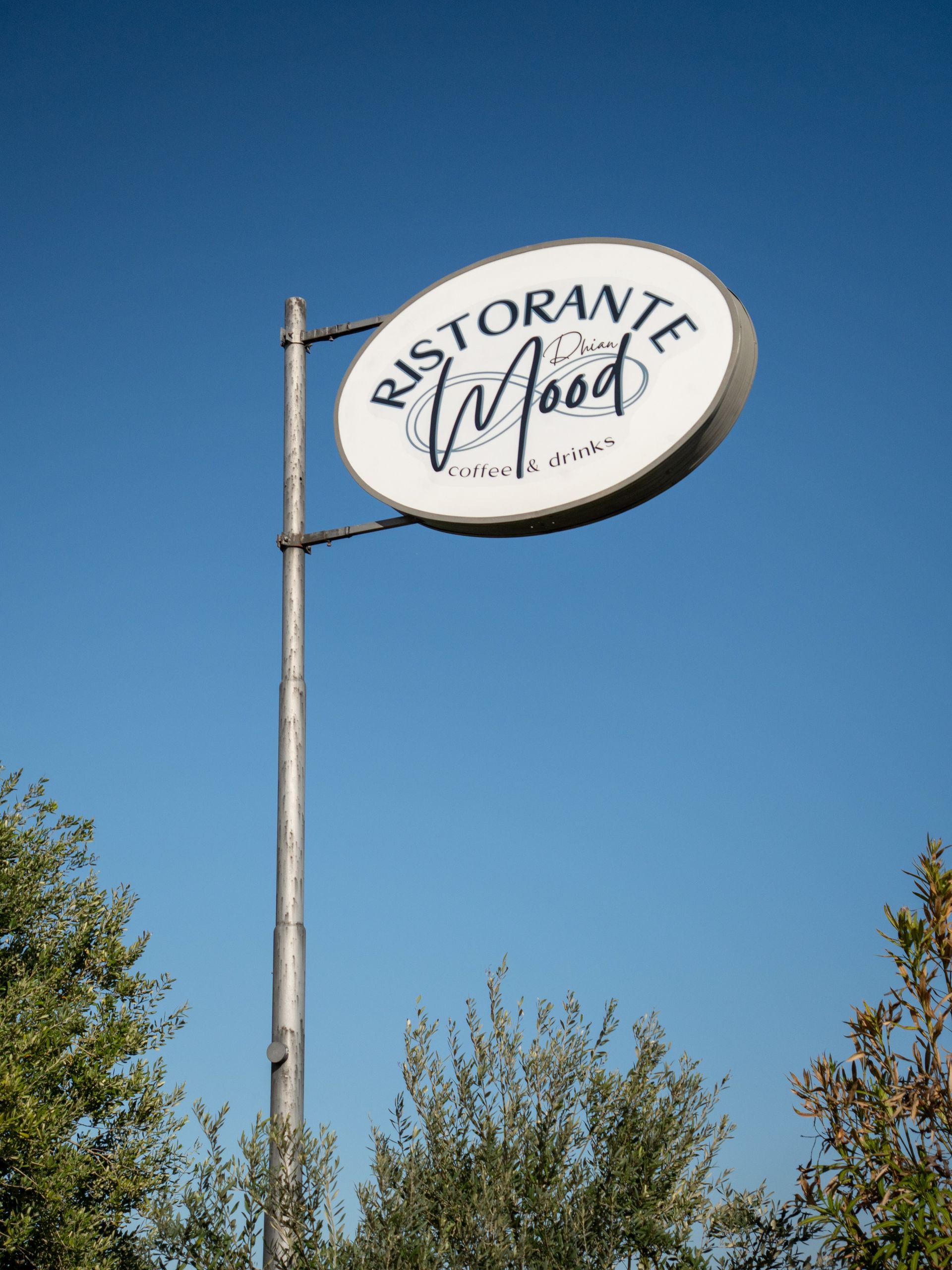 Insegna di un ristorante su un palo, stagliata contro un cielo azzurro limpido sopra gli alberi.