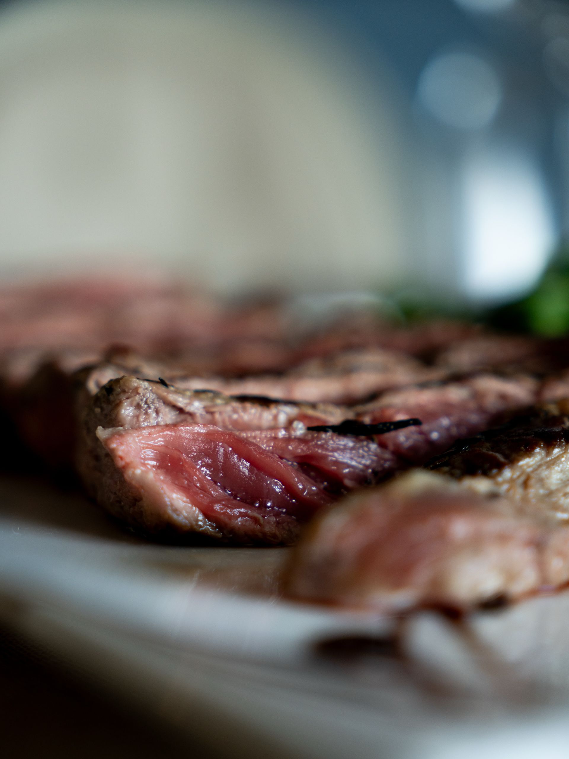 Una bistecca al sangue tagliata a fette su un piatto, con uno sfondo sfocato.