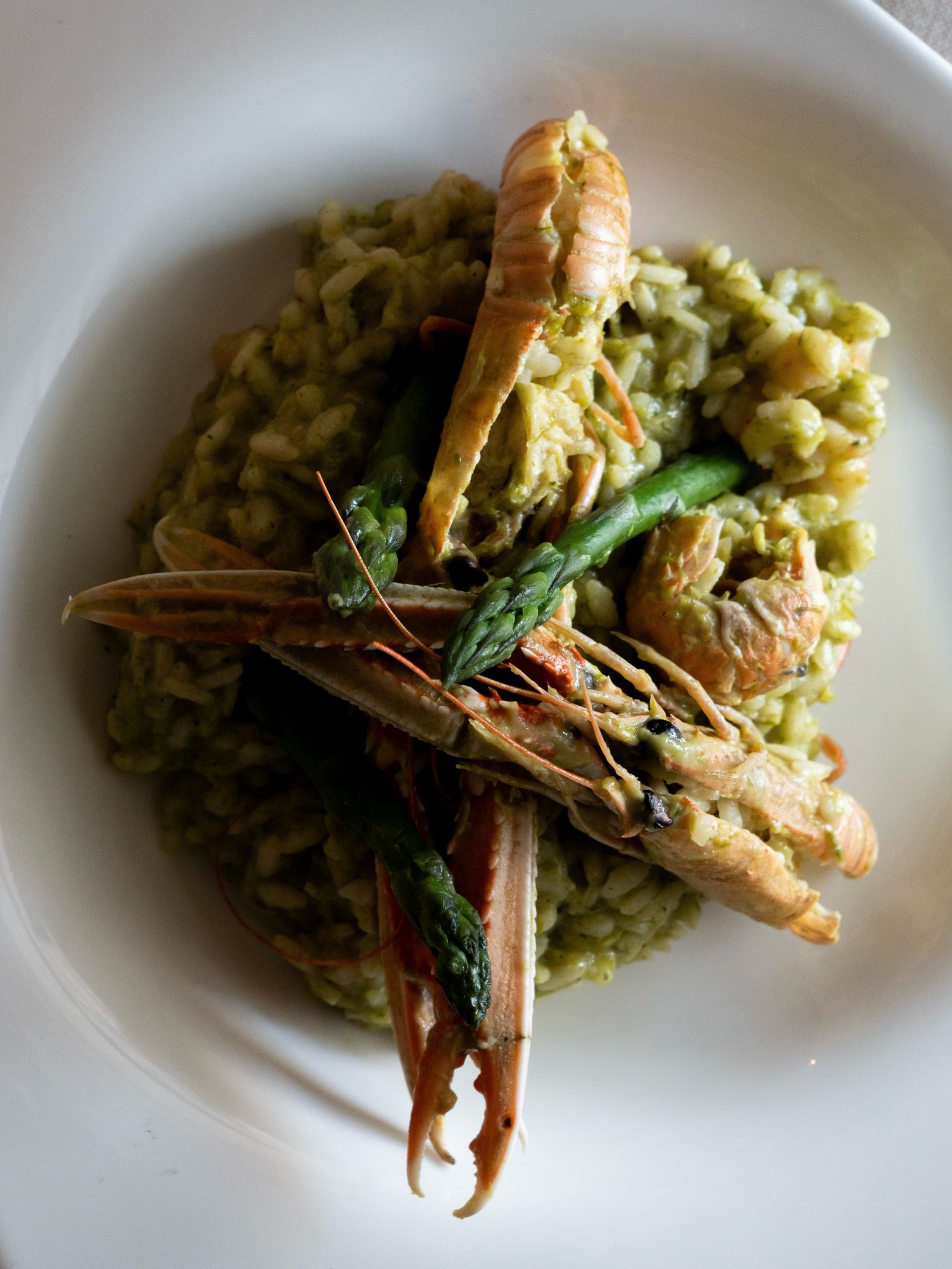 Piatto di risotto verde con gamberi e fagiolini in una ciotola bianca.