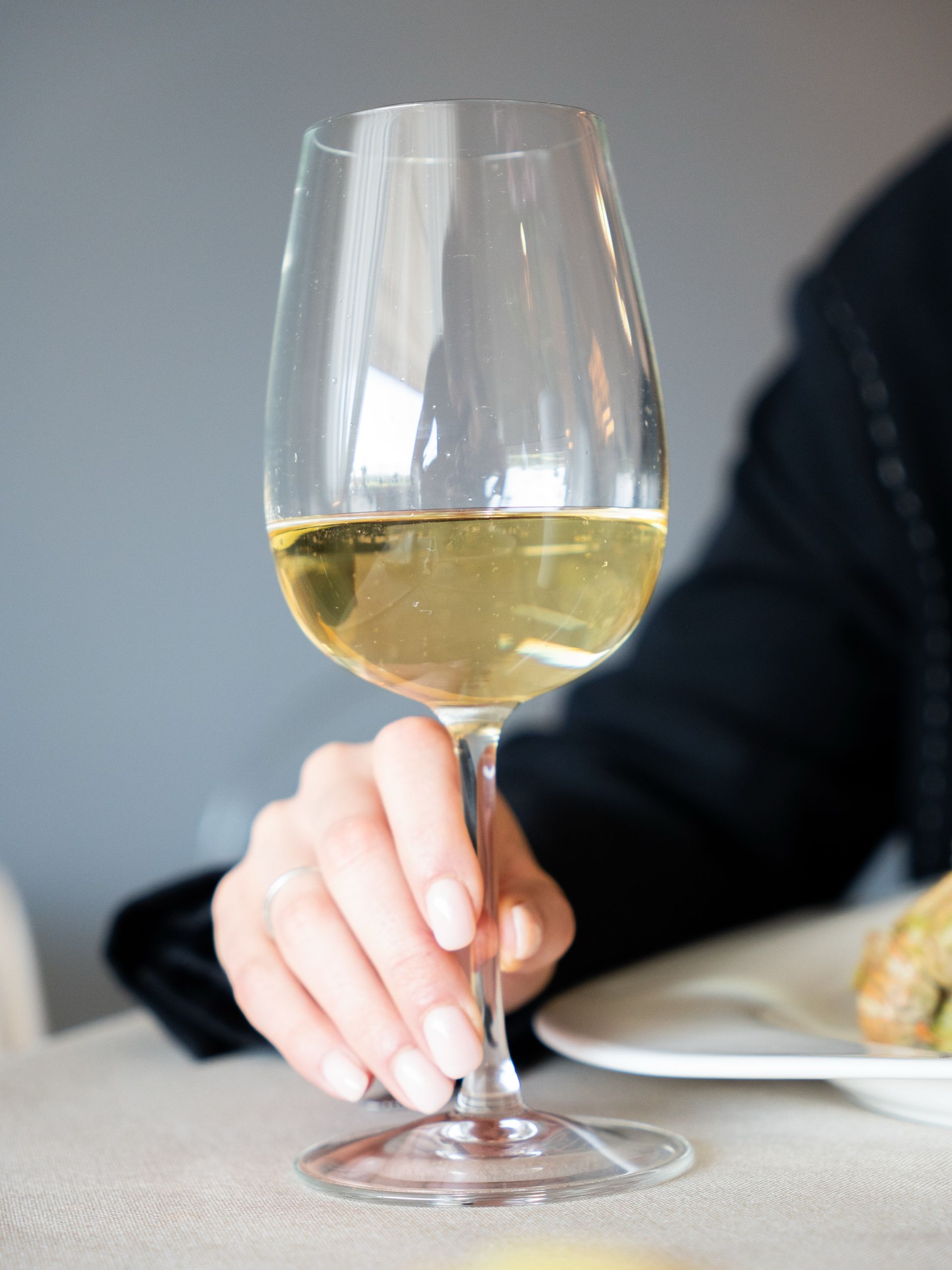 Mano che regge un bicchiere di vino bianco a un tavolo da pranzo