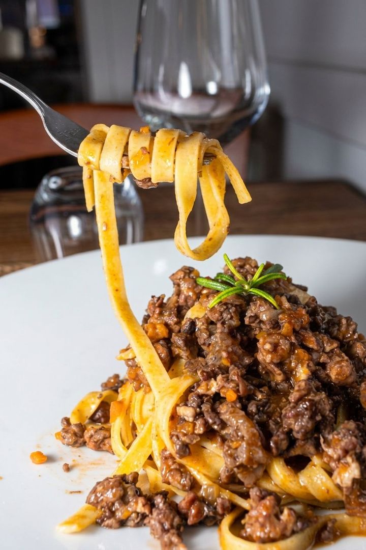 Pasta al ragù servita su una forchetta sopra un piatto bianco in un ristorante.