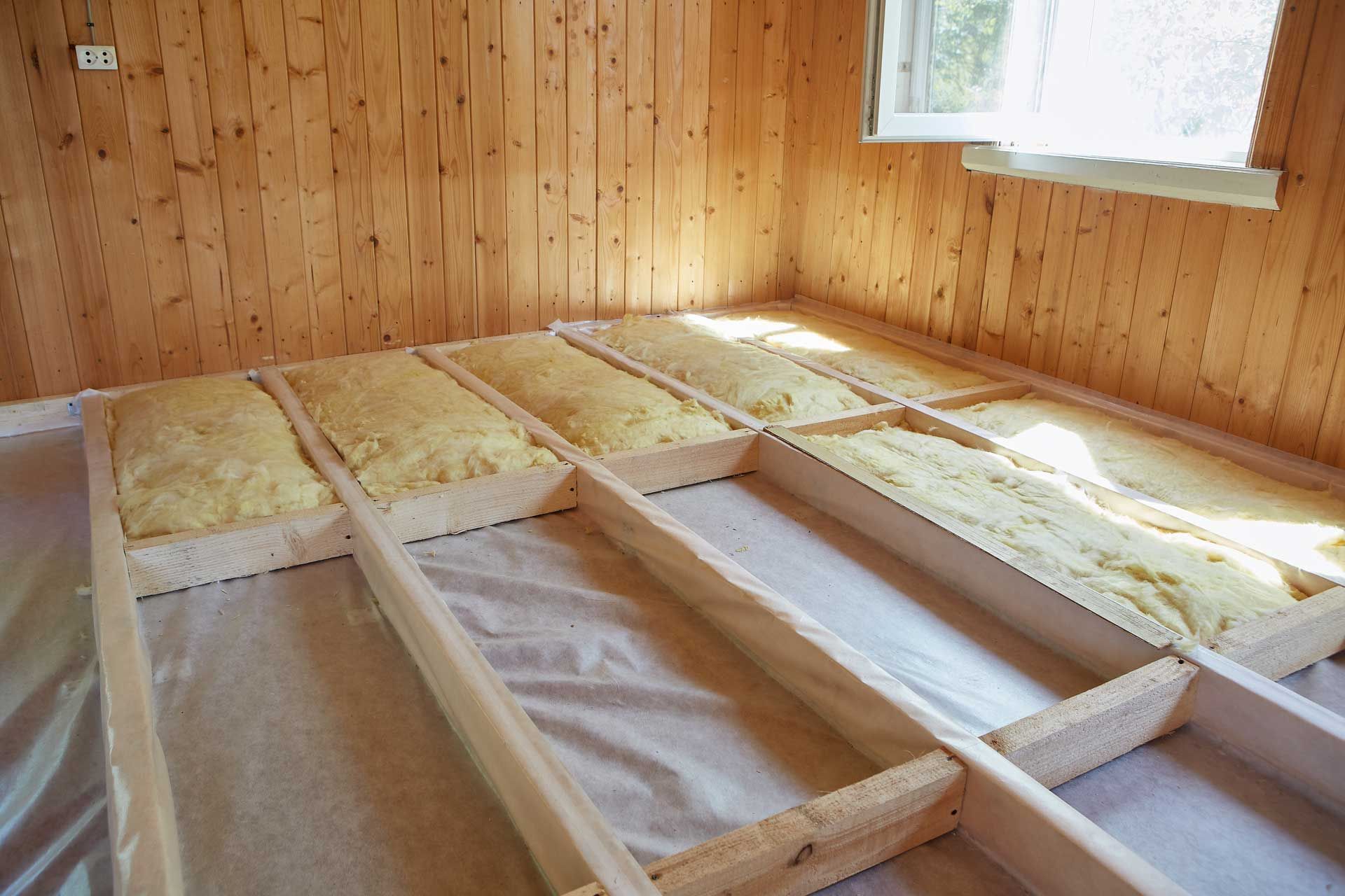 Wooden floor framing with insulation, a partial view of a room.