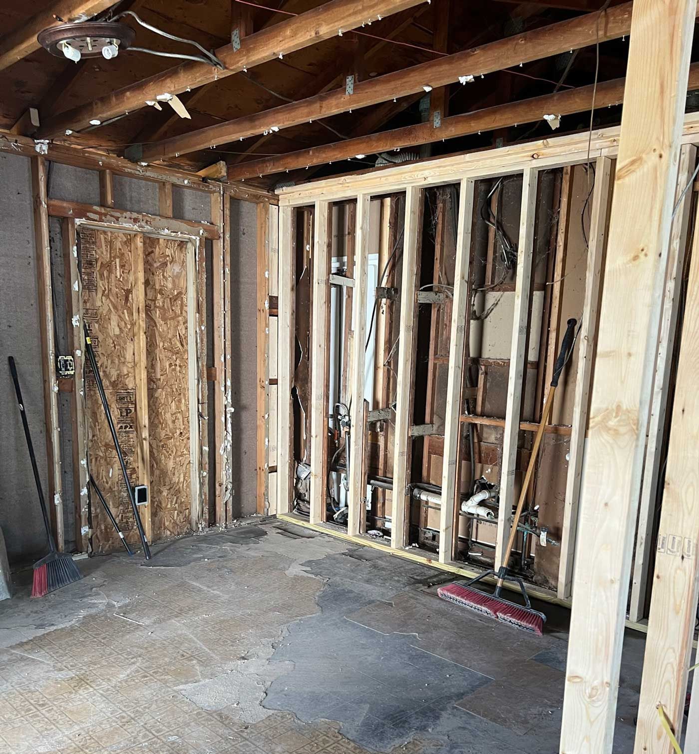 Interior framing and demolition of a room. Wood beams and studs visible; electrical wiring and a door frame. Interior framing and demolition of a room. Wood beams and studs visible; electrical wiring and a door frame.