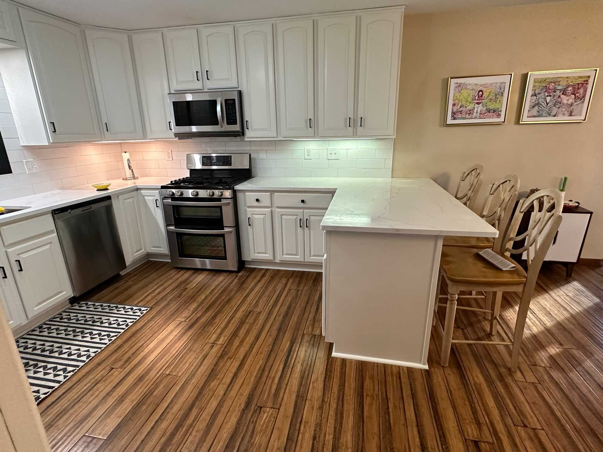 White kitchen with stainless steel appliances, white cabinets, island with stools, and wood flooring.