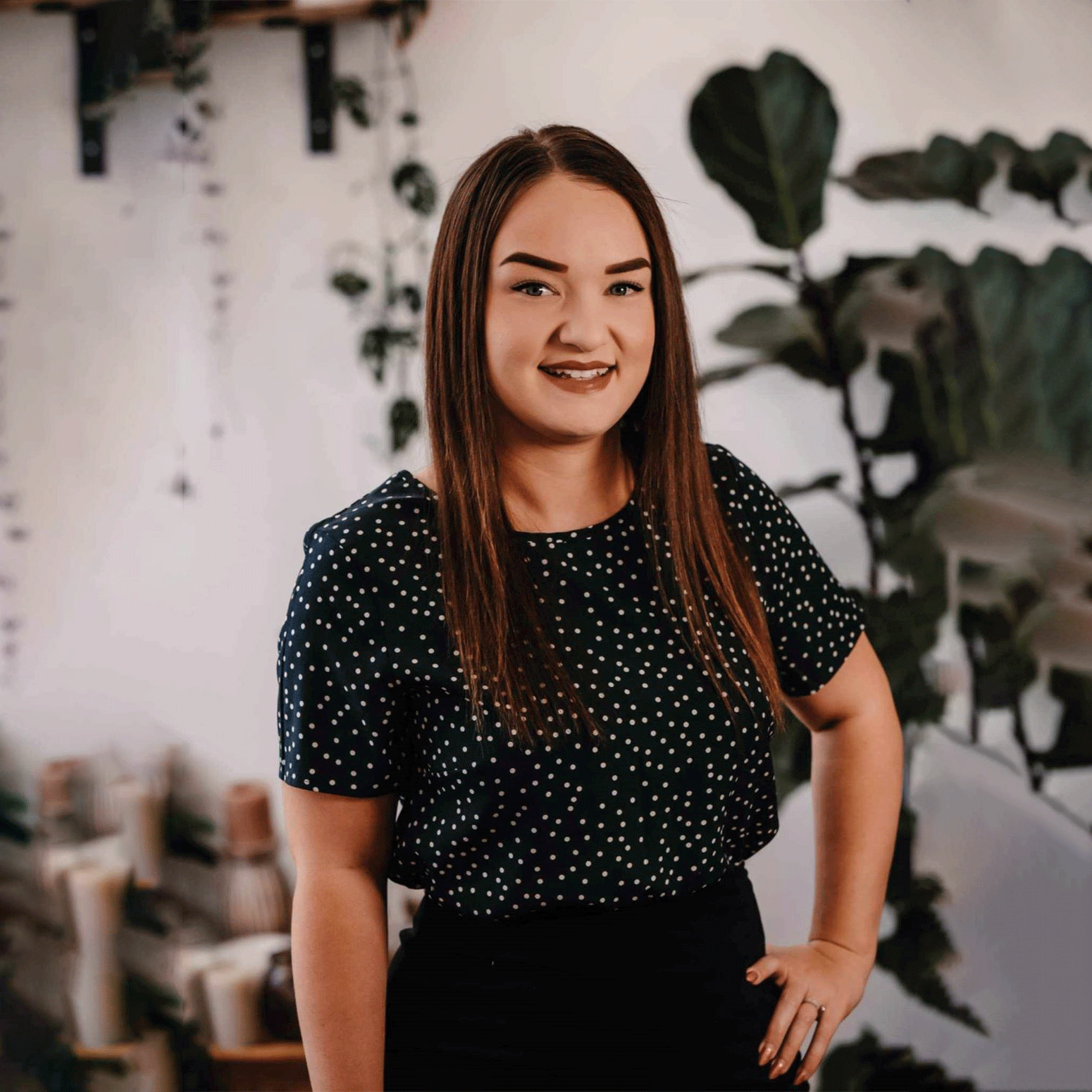 A woman in a polka dot shirt is standing in front of a plant.