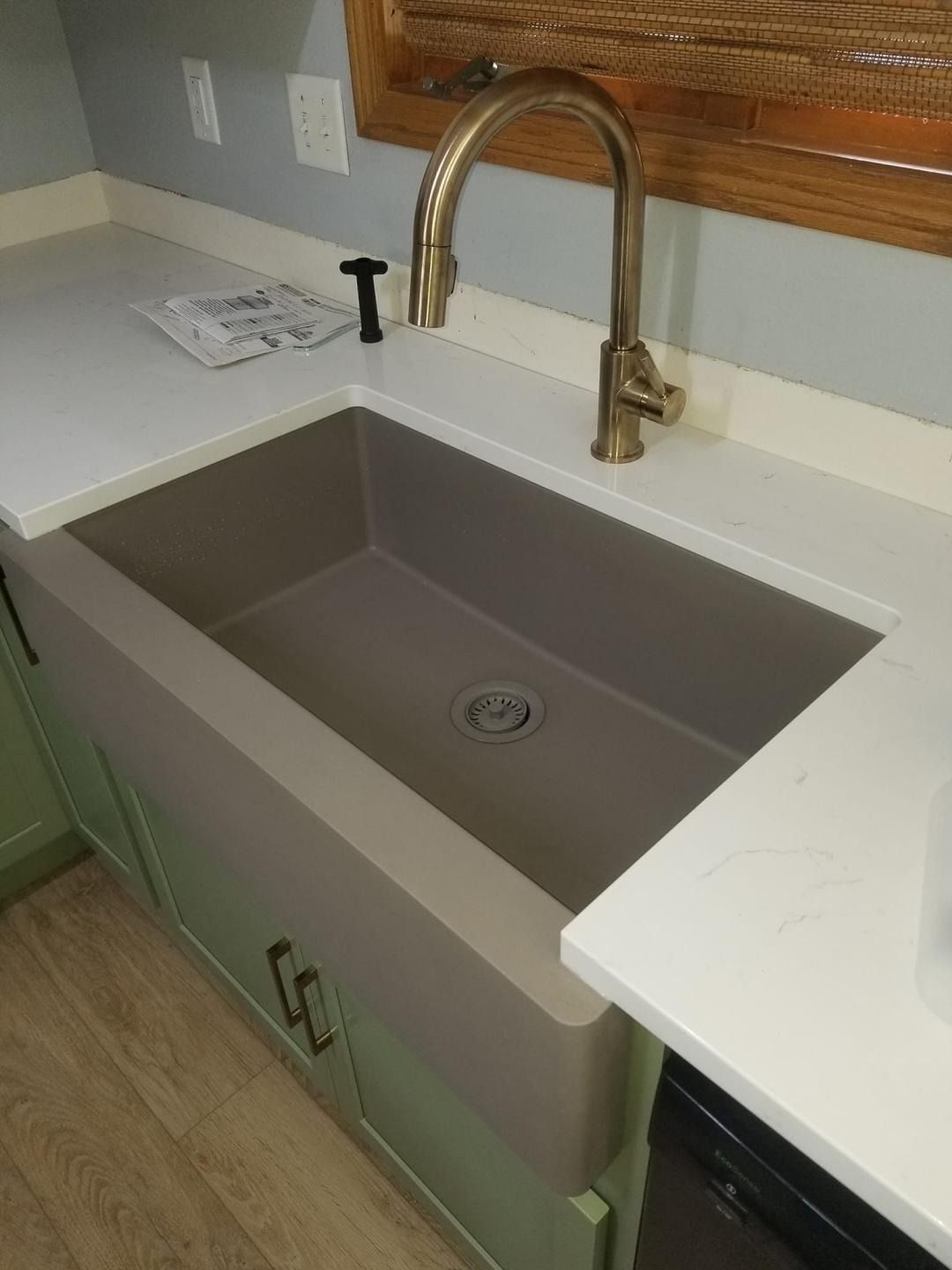 Gray farmhouse sink with brass faucet and white countertop in a kitchen