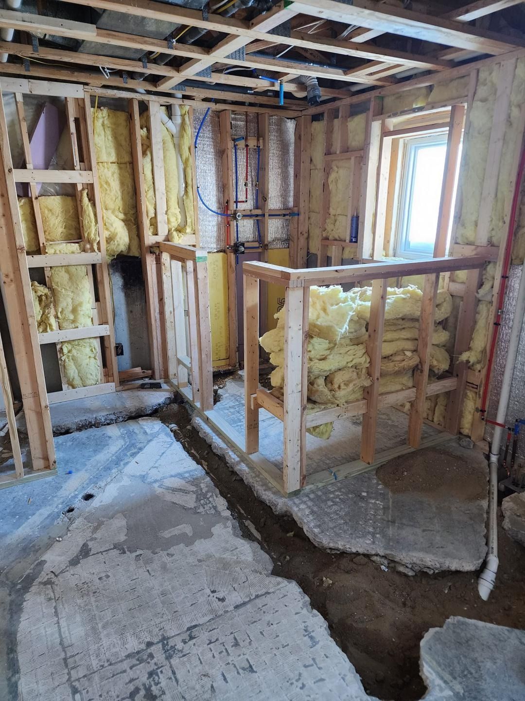 Partially renovated room with exposed framing, insulation, and unfinished floor walls