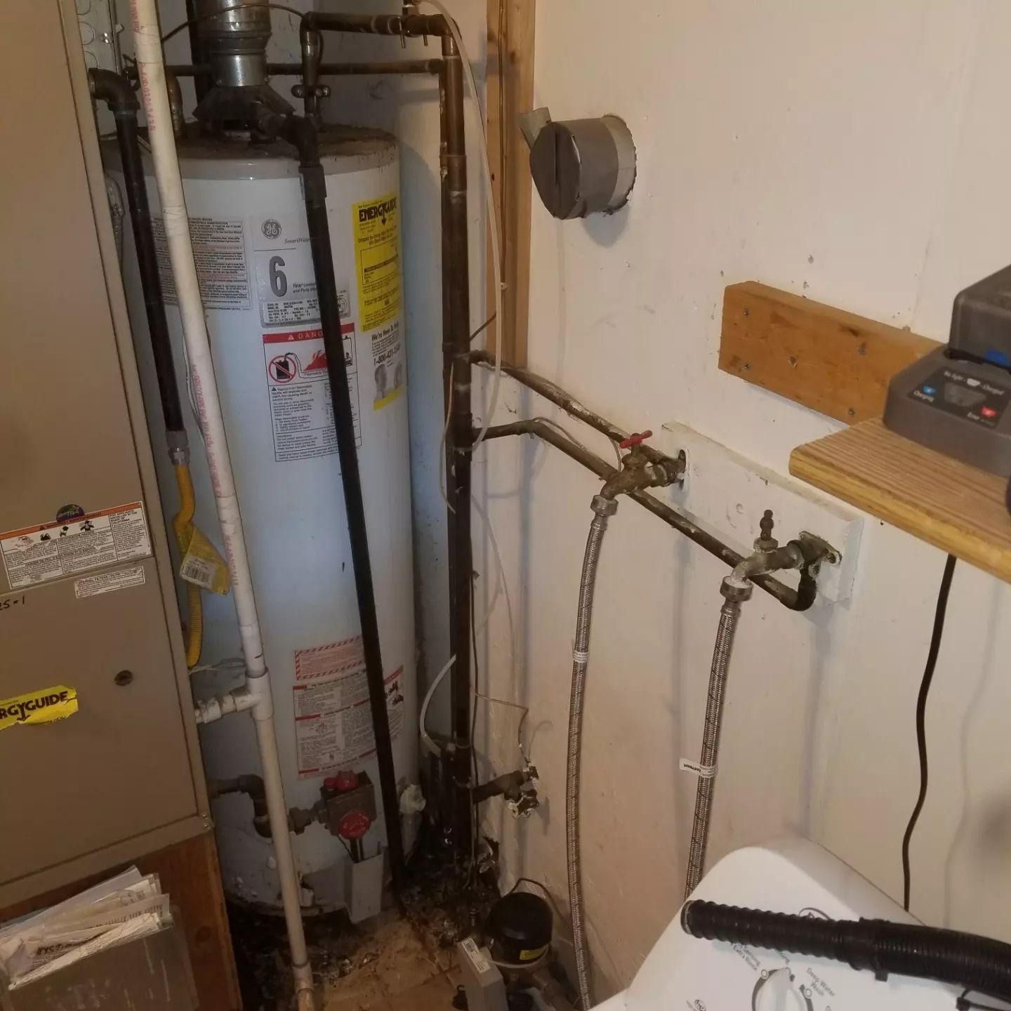 Utility room with two water heaters, exposed pipes, and a wall-mounted electrical meter.