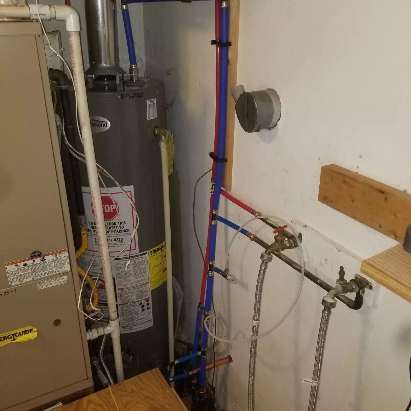Utility room with water heater, furnace, and exposed plumbing pipes against a wall.