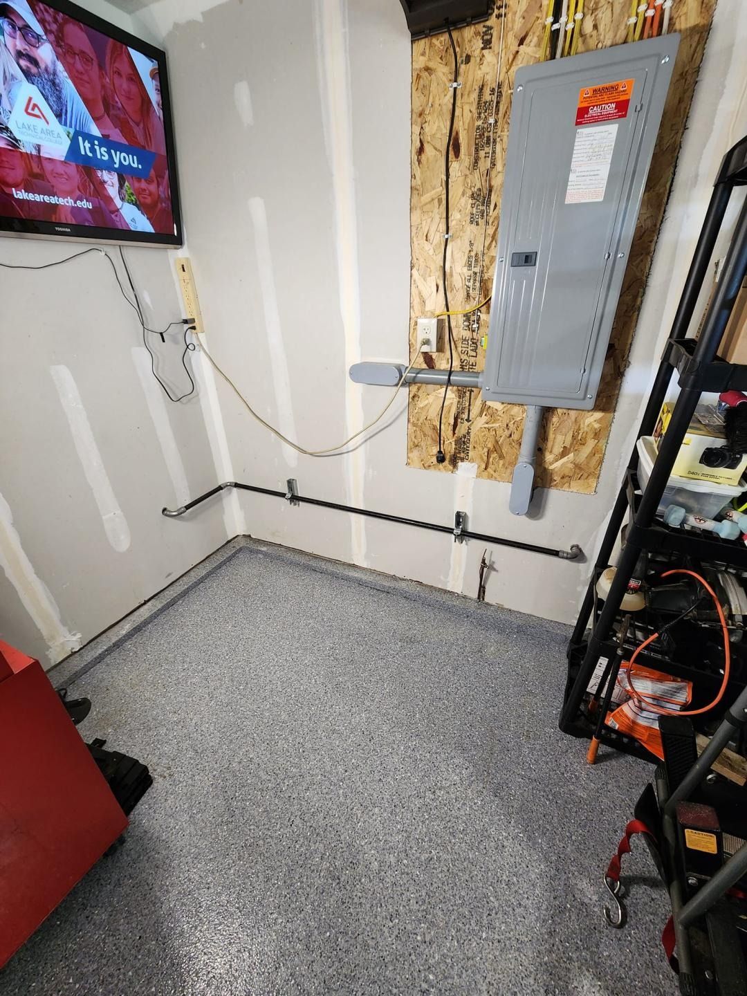 Utility room corner with electrical panel, exposed wiring, and gray speckled floor carpet.