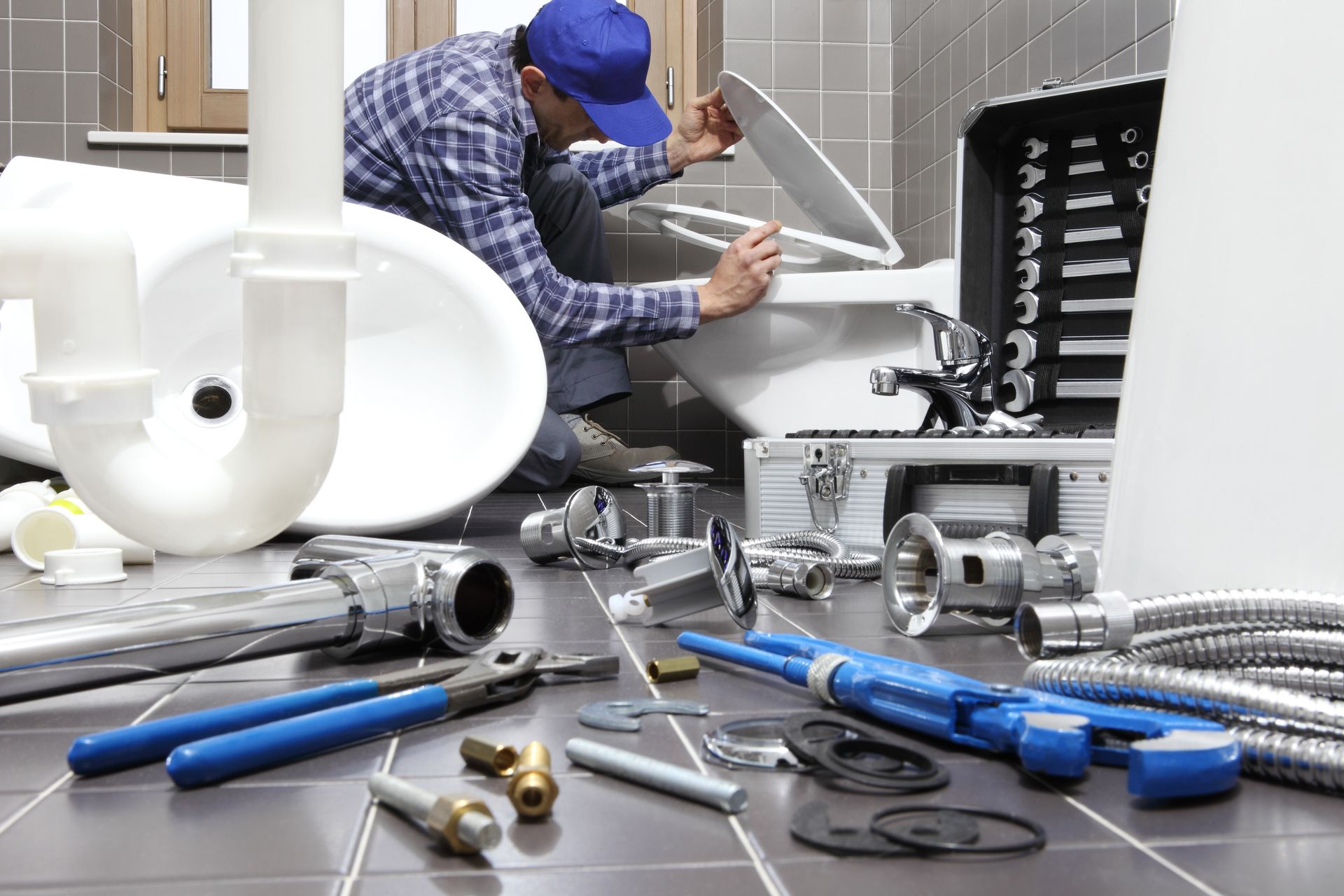 Plumber repairing a sink under a counter, with tools scattered across the floor.