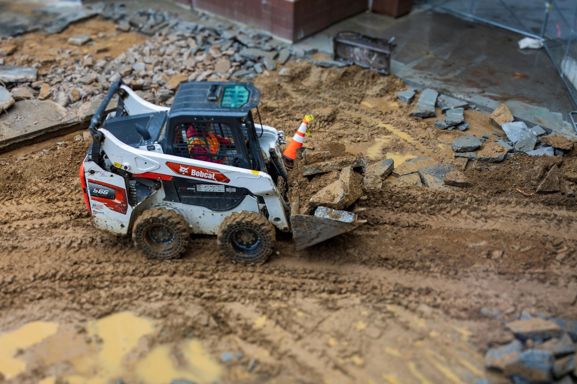 Bobcat skid-steer loader scooping dirt and debris on a construction site.