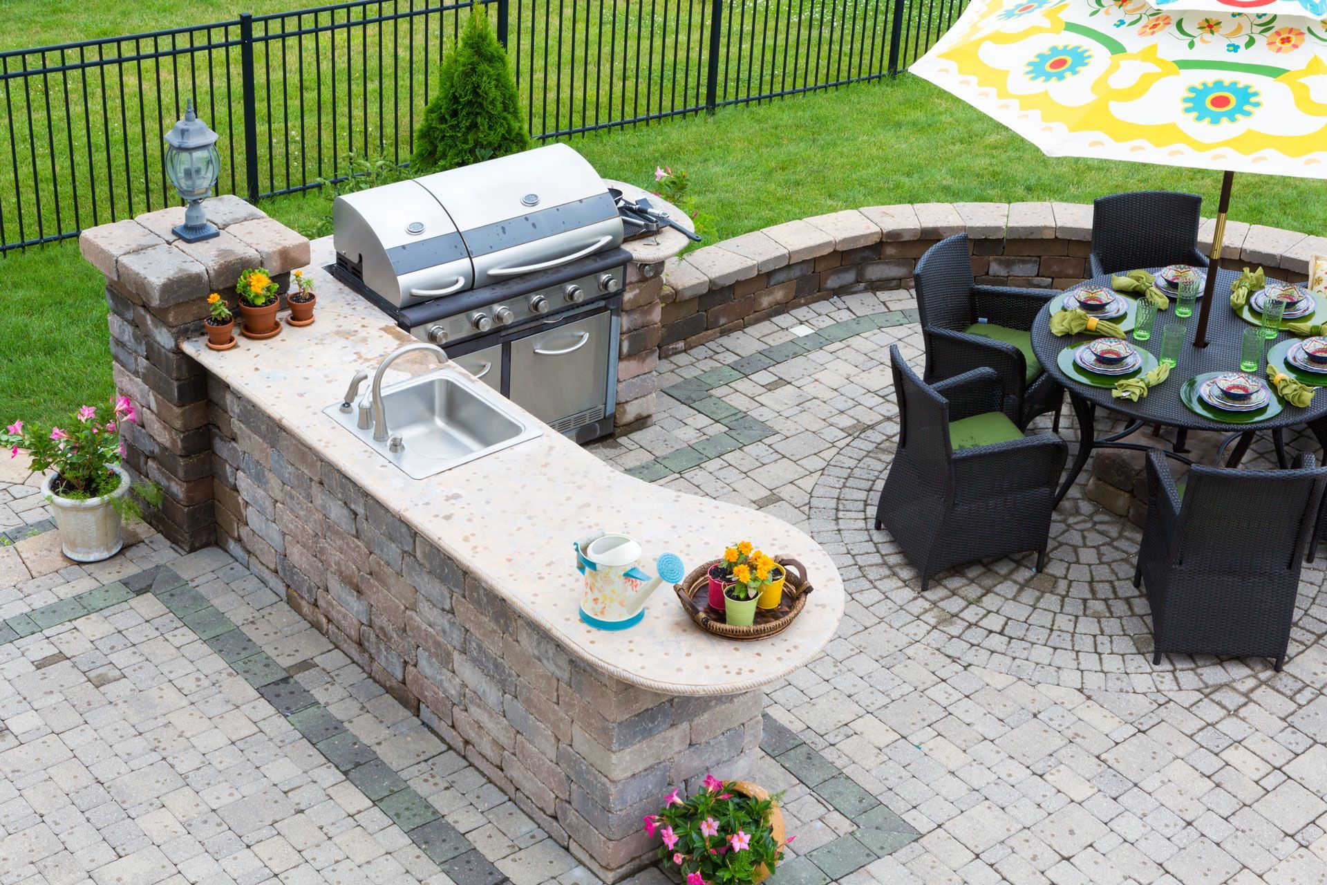 Outdoor kitchen with grill, sink, and countertop seating area; adjacent dining table under umbrella.