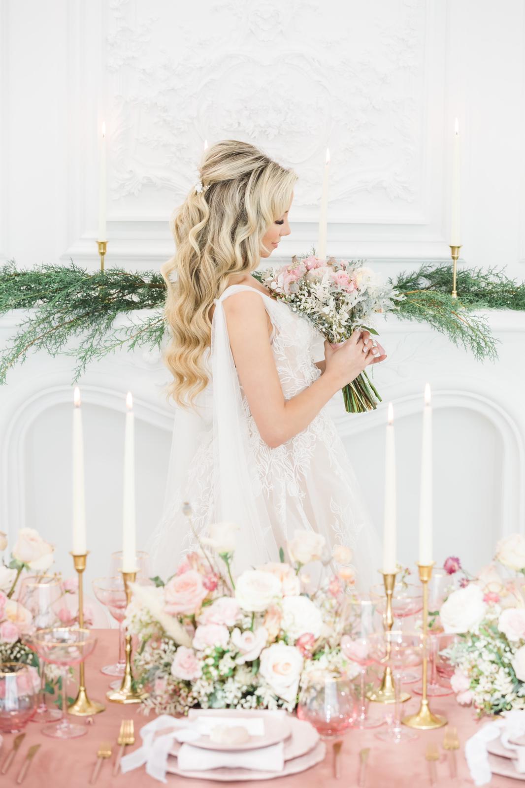A bride is standing in front of a table with flowers and candles.