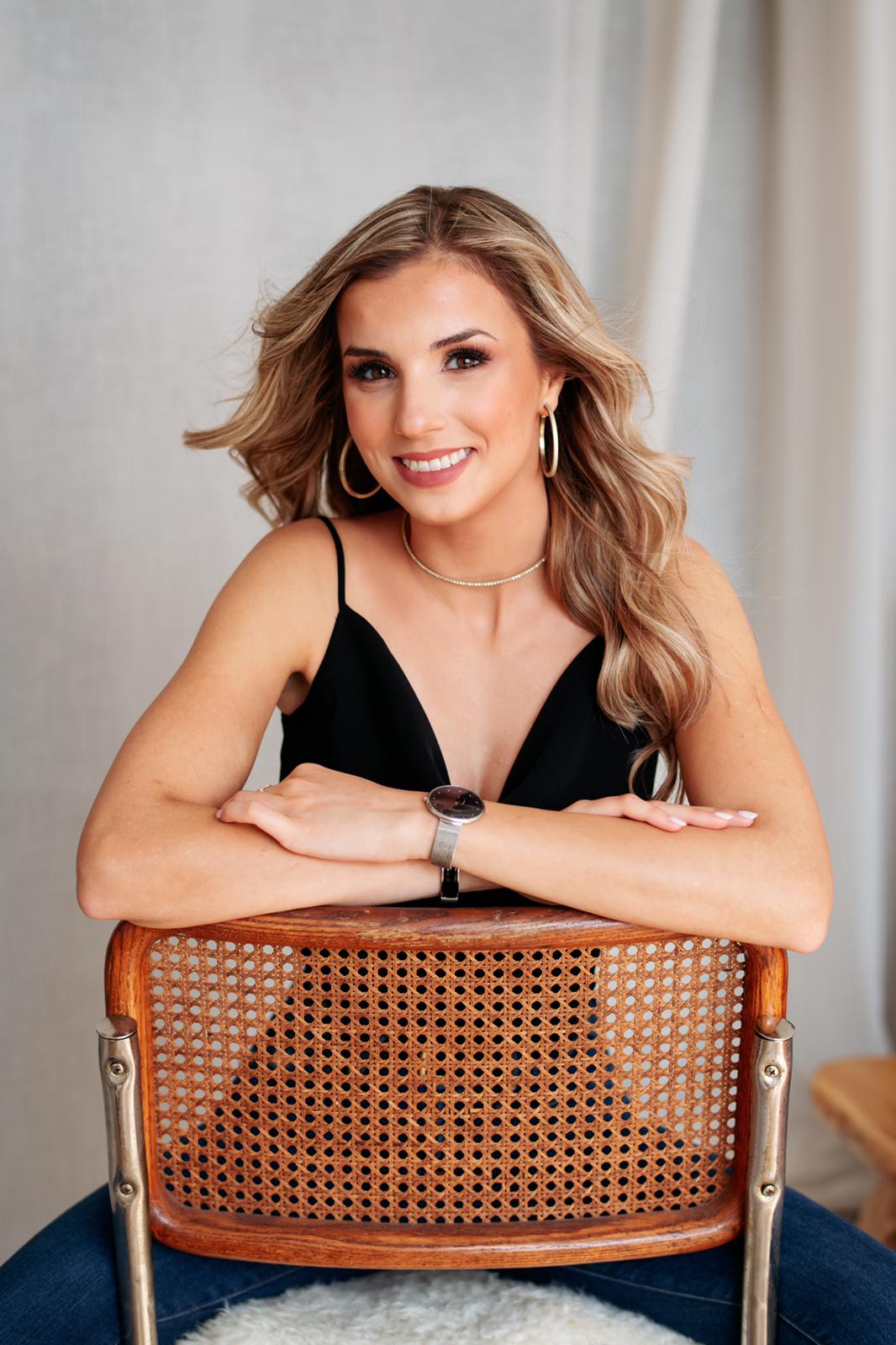 A woman is sitting in a chair with her arms crossed and smiling.